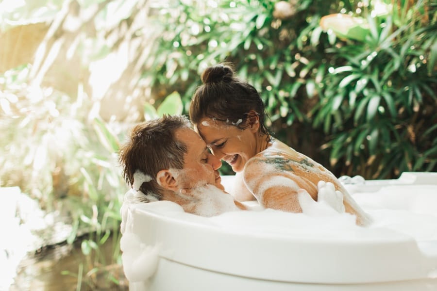 Lovely pretty couple enjoying together in outside bathtub full ou foam bubbles. Romantic honeymoon in Asia